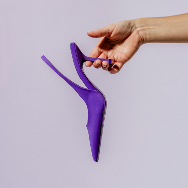 Purple high heeled pump held over a lavender background
